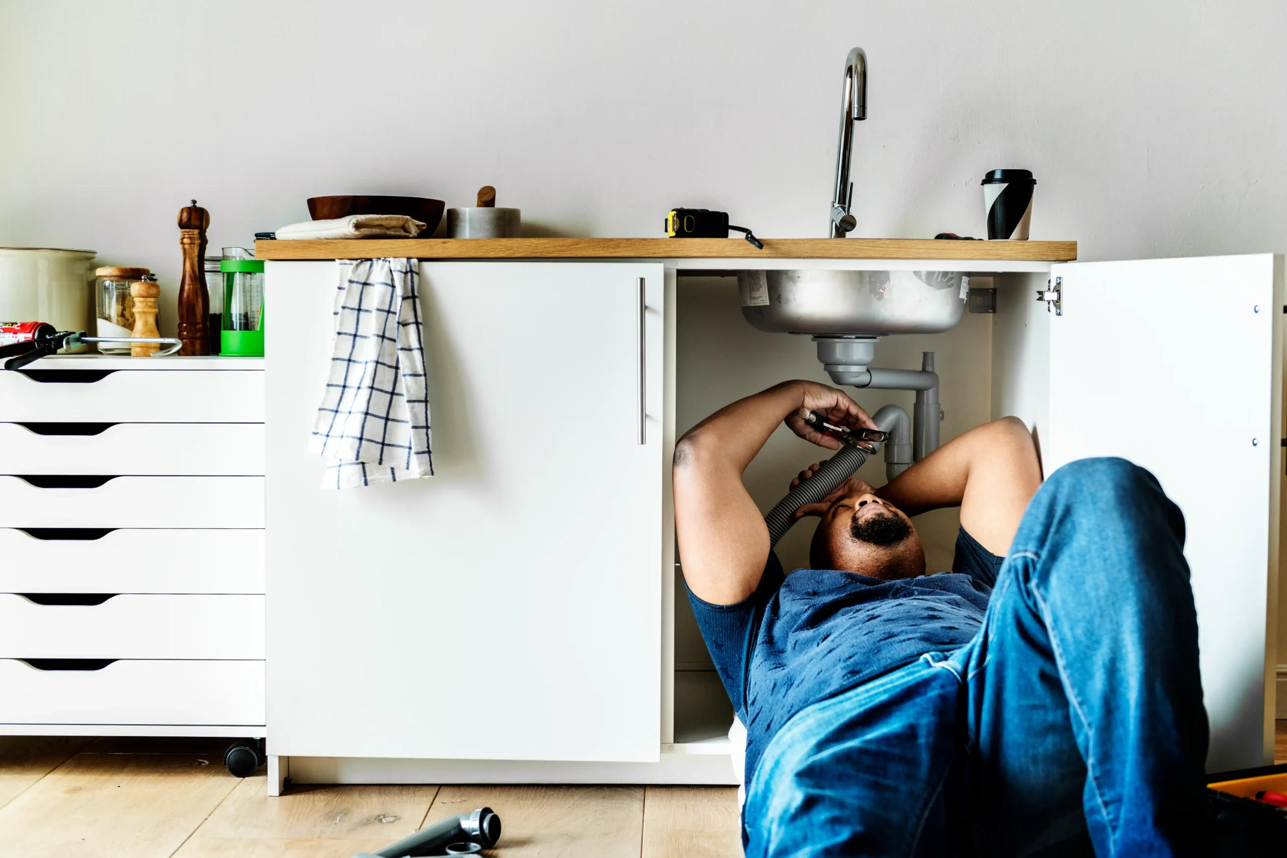Plombier Namur allongé au sol effectuant une réparation sous un évier de cuisine